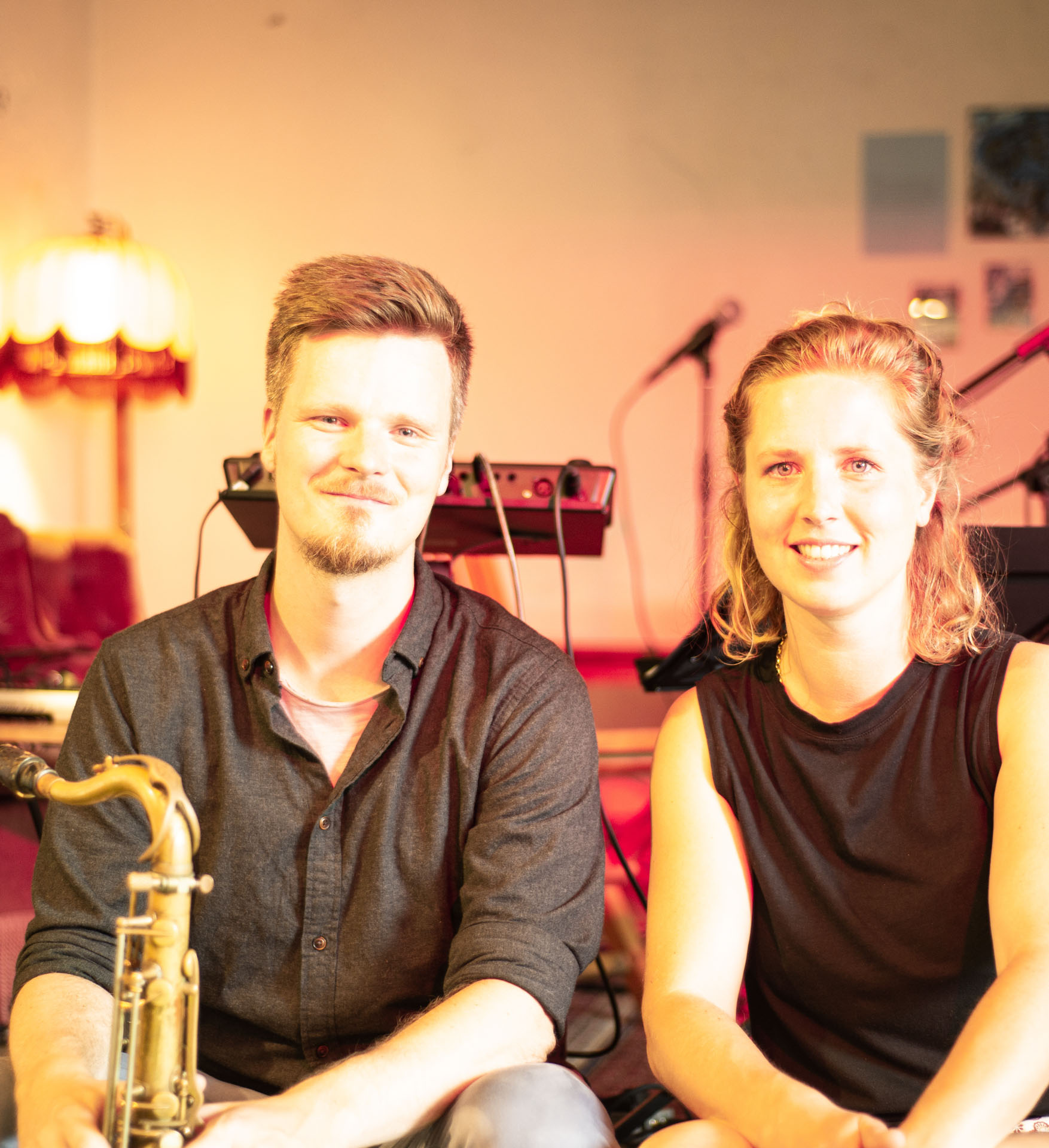 Paul und Romy sitzen nebeneinander vor der Bühne des Café Leitstelle. Paul hat ein Saxophon in der Hand (Bild: Leading Edge).